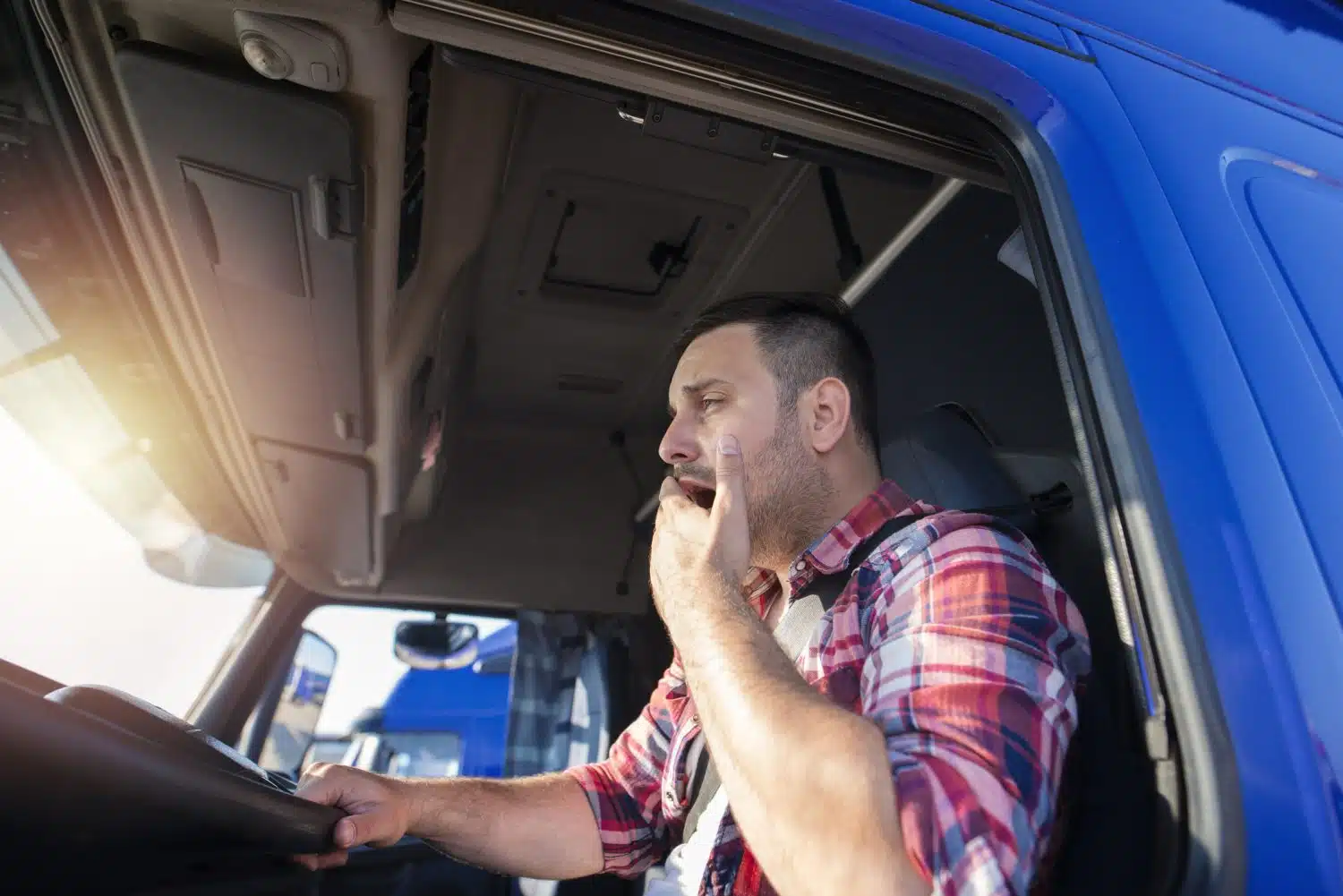 A truck driver yawns behind the wheel indicating drowsy driving.
