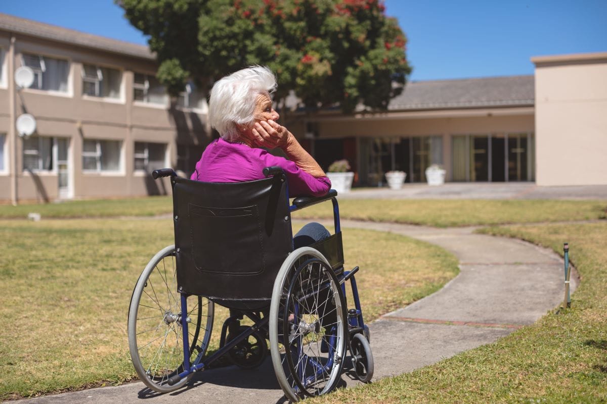 Arkansas woman in wheelchair sits alone in nursing home courtyard.